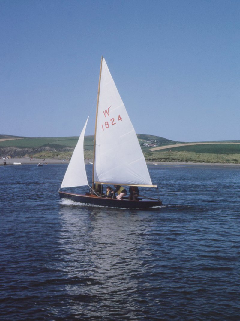 A dinghy under sail. We see the beach in the background. The dinghy's number, W1824, is prominent