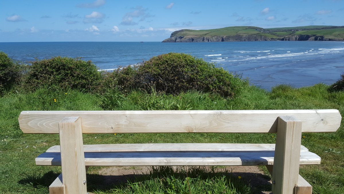 The back of a bench is in the foreground showing its view across a broad bay
