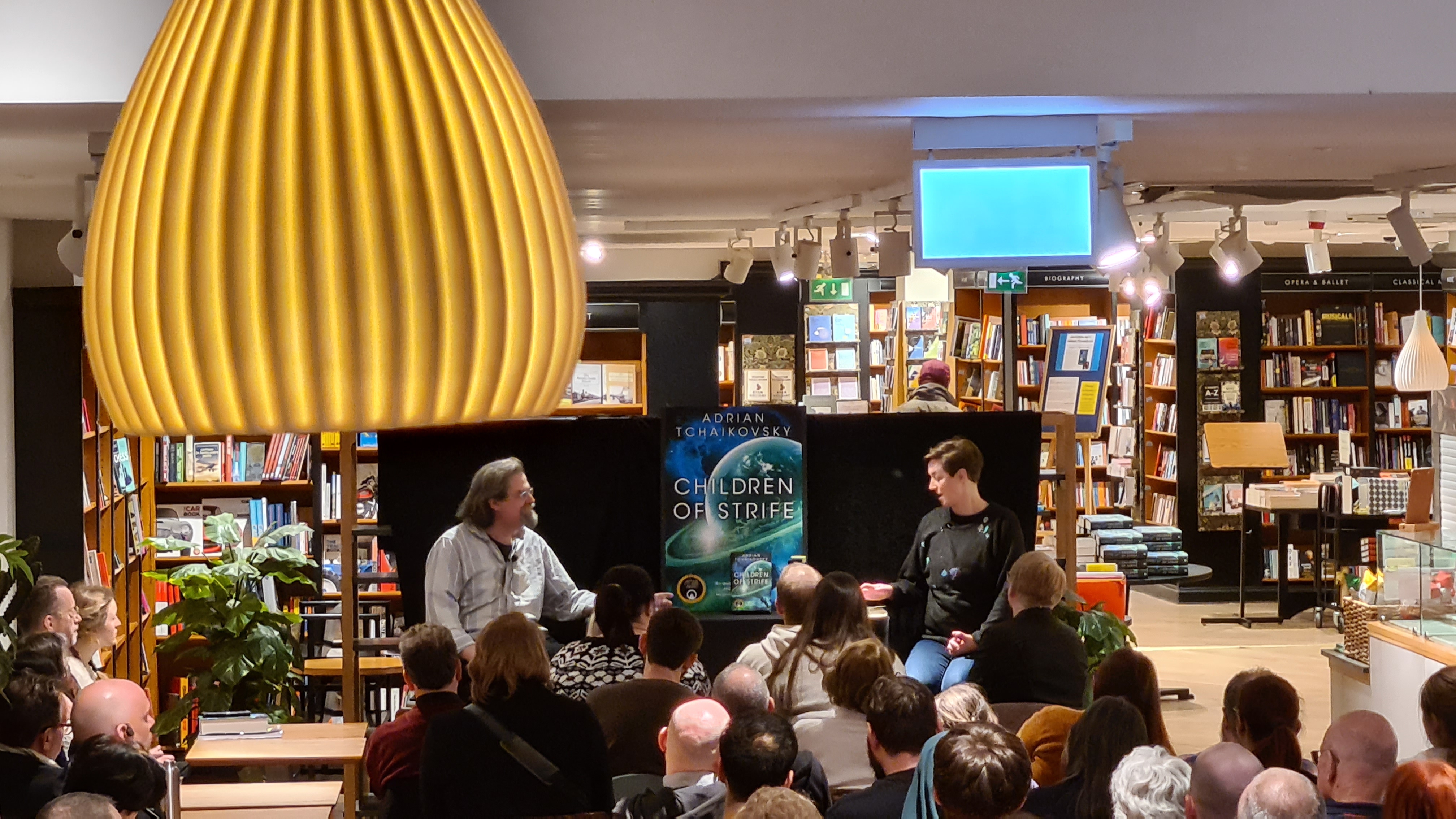 The view of the event right from the back of the room. Seated at the front are Adrian Tchaikovsky and Claire North.