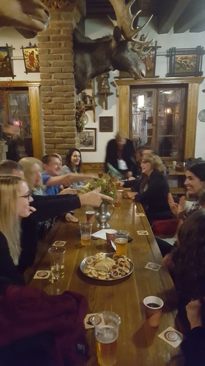 A group of adults sit around a pub table, laughing and pointing accusatorily at each other