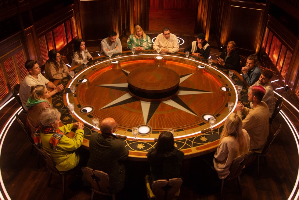 16 people sitting at a large round table that looks a little like a static roulette wheel