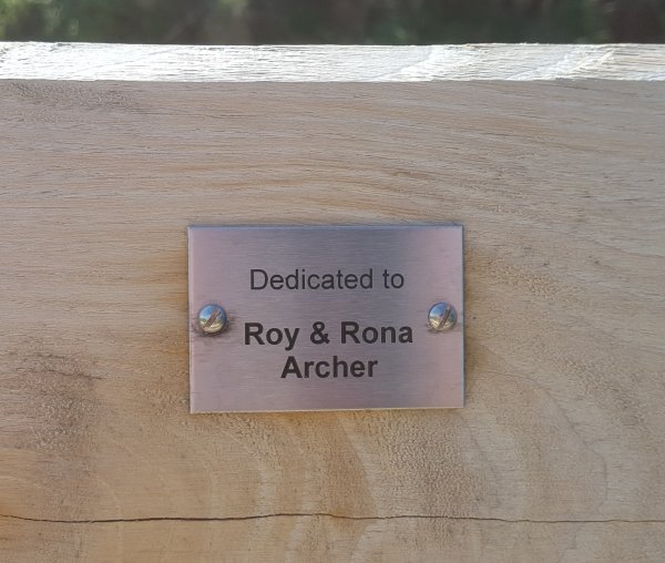 Small silver plaque mounted on wood engraved with the dedication to Roy and Rona Archer
